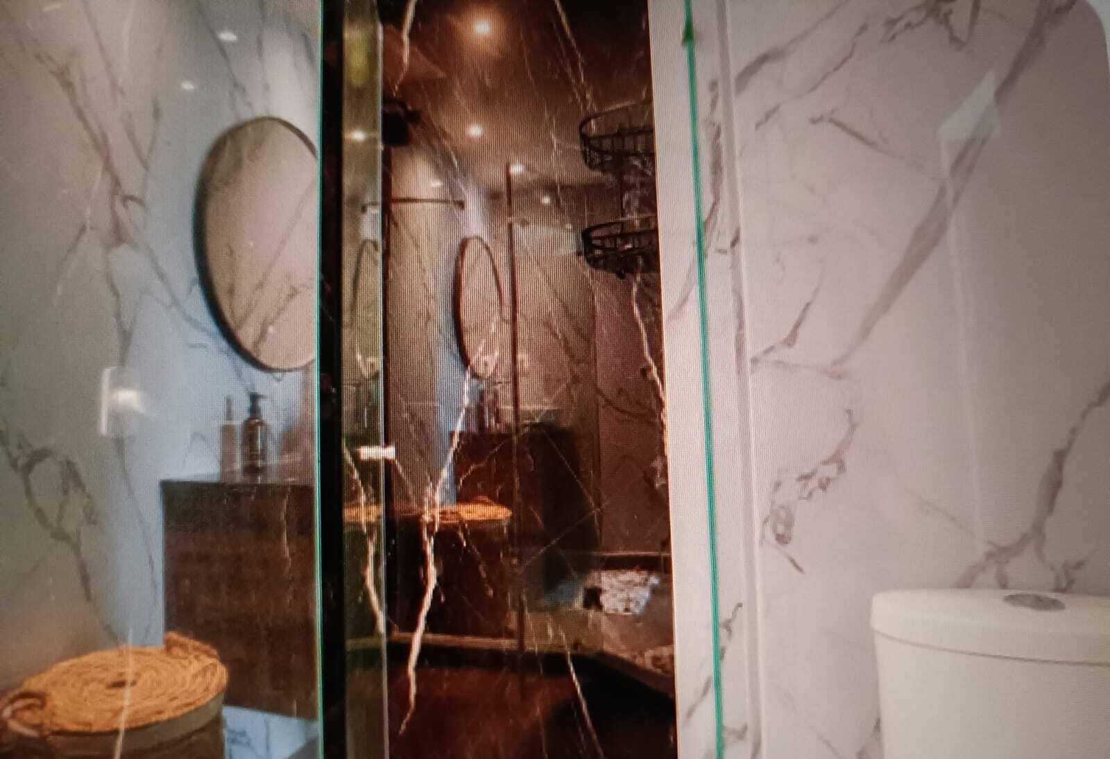 Une salle de bain avec un mur en marbre, un miroir rond, un tabouret en bois et des toilettes.