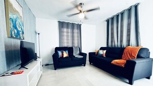 Uma sala de estar moderna com dois sofás pretos, uma televisão de tela plana e um ventilador de teto.