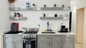 Cozinha moderna com fogão a gás, forno e máquina de café. Há prateleiras com utensílios básicos de cozinha e objetos decorativos.