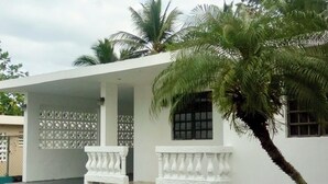 Um edifício branco com varanda coberta, palmeiras e cerca decorativa.