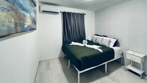 Quarto com cama, mesa de cabeceira, ar condicionado na parede, um quadro e uma luminária de teto.