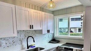 A modern kitchen with white cabinets, a hexagonal tile backsplash, a stainless steel sink, a black stove, and a hanging light fixture.