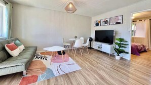 A modern living room with a sofa, a dining table, a TV, and a ceiling light fixture.