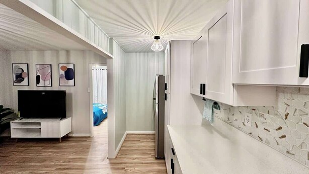 A modern kitchen with white cabinetry, a built-in TV, and a unique ceiling light fixture.