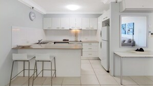 A modern kitchen with white cabinetry, a central island with stools, a built-in oven, and a refrigerator. - Beachside 1BR Ocean View Apartment with Parking (Broadbeach)