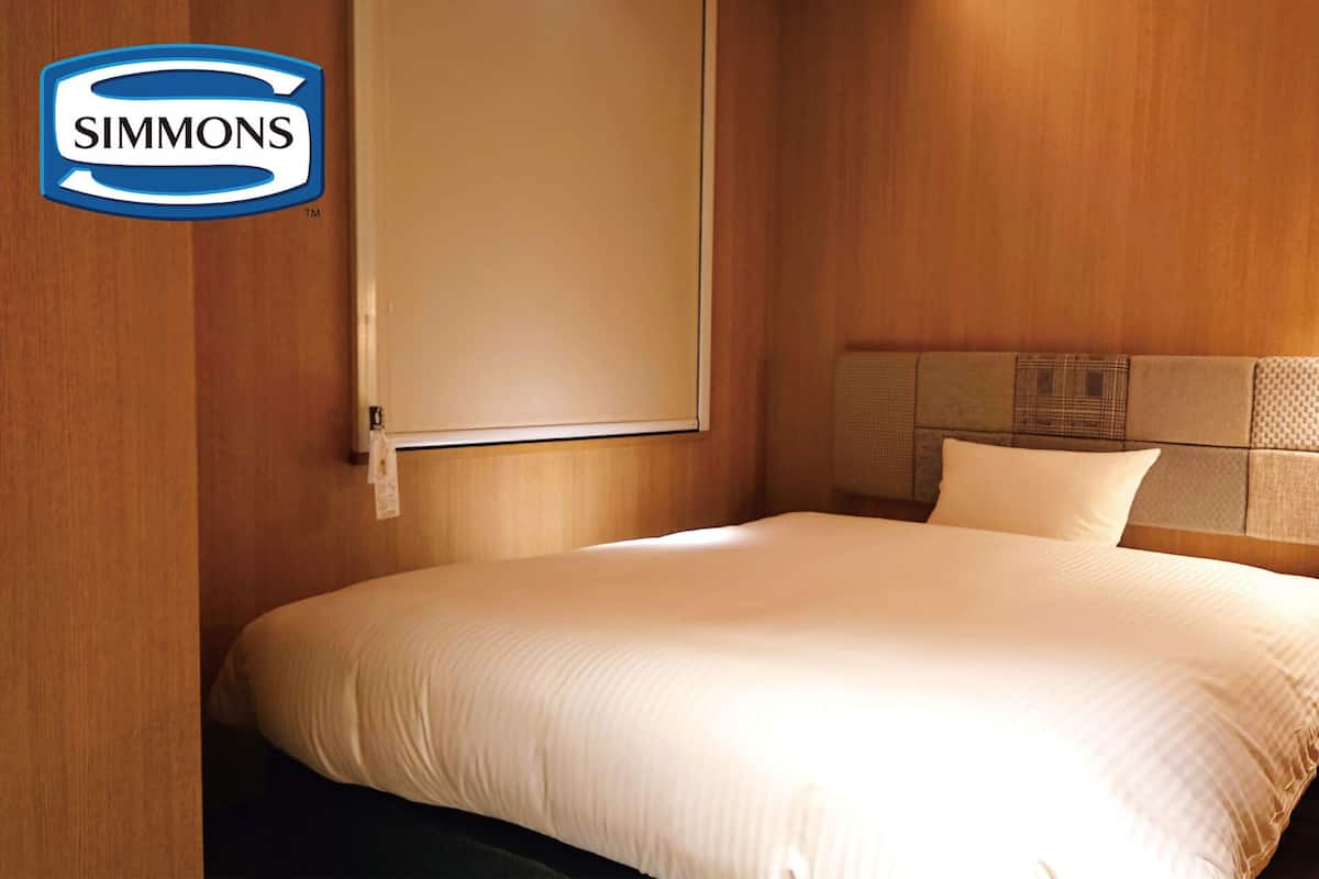 Ett hotellrum från Simmons med en säng, ett nattduksbord, en lampa och en sänggavel med en strukturerad panel.