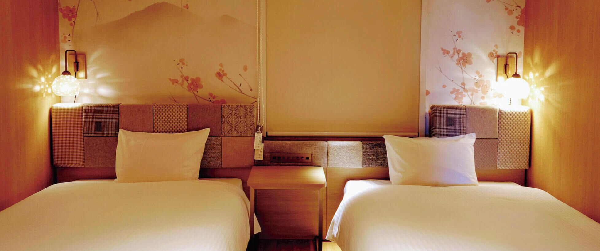 Une chambre d’hôtel avec deux lits, une table de chevet, une lampe fixée au mur et un panneau décoratif mural.