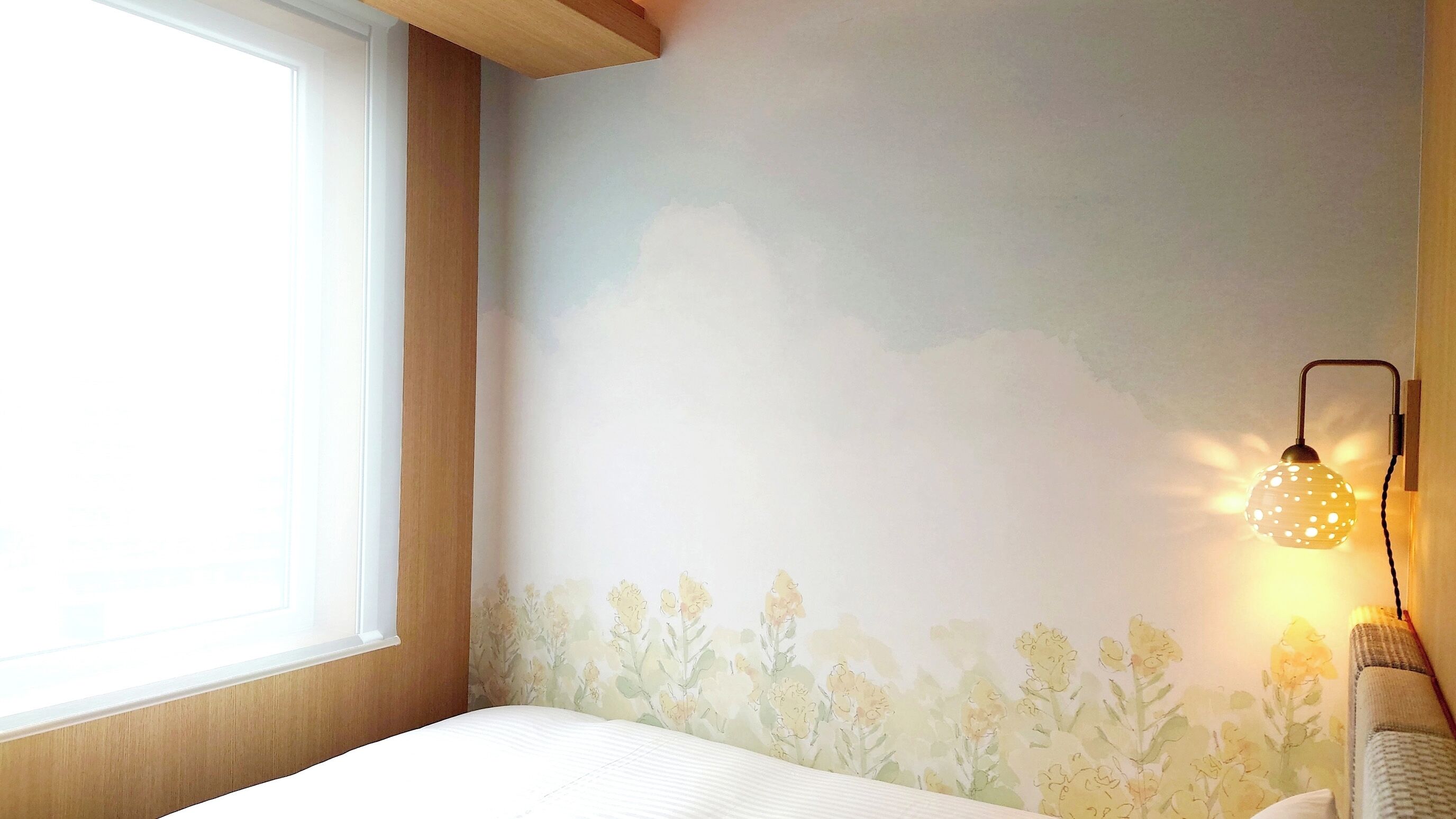 A bedroom with a large window, a wall-mounted lamp, and a floral wallpaper design.