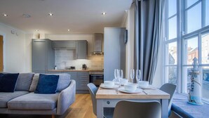 Una cocina moderna con armarios grises, una mesa de comedor preparada para cuatro personas y vistas de la ciudad a través de amplios ventanales.