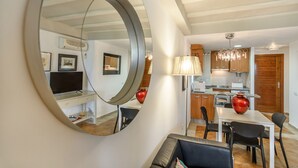 A modern living room with a circular mirror, a dining area with a table and chairs, and a kitchen with wooden cabinets and a chandelier.