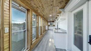 Un pasillo con paneles de madera y ventanas amplias, que conduce a una zona de cocina con armarios blancos y una encimera.