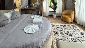 Une chambre d’hôtel moderne avec un grand lit, un coin salon avec un fauteuil, un bureau et une plante en pot.