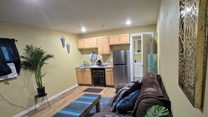 Un espacio habitable compacto con kitchenette, un sofá marrón, una mesa de centro y una planta en maceta.