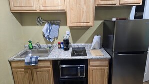 Una cocina con armarios de madera, un refrigerador de acero inoxidable, un microondas, un lavamanos y una pequeña encimera con varios objetos.