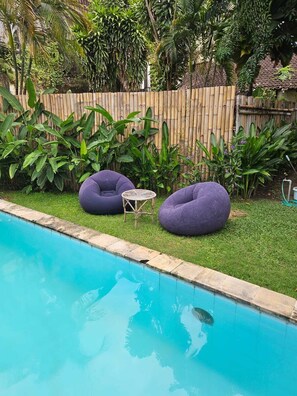 A swimming pool with two purple bean bag chairs and a small table. - Two Brothers Guesthouse (Legian)
