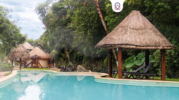 A pool area with thatched-roof structures, lounge chairs, and a slide. - Apt with Pool & jungle in Puerto Morelos (Puerto Morelos)