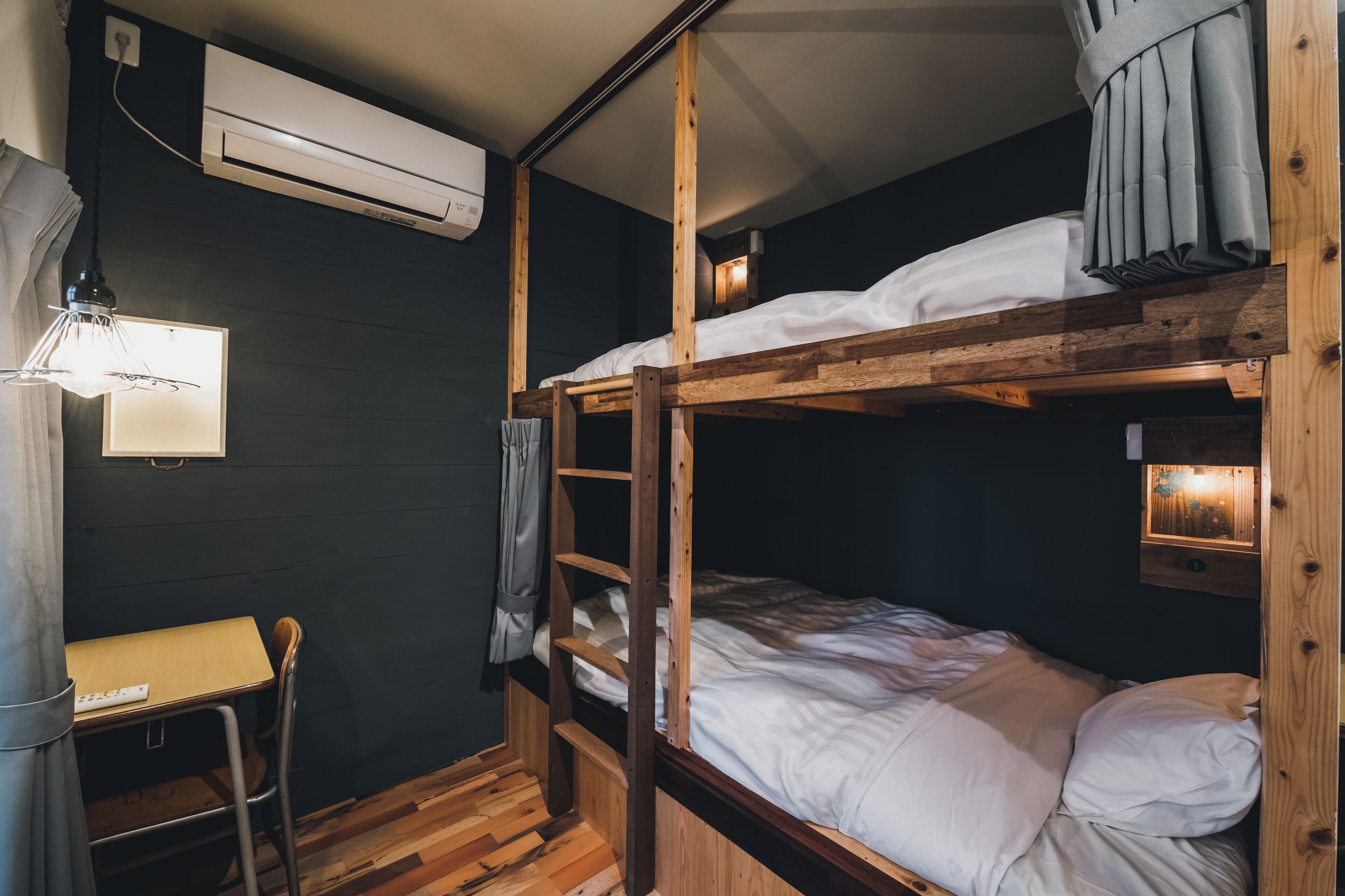 Habitación con literas, escritorio, silla, unidad de aire acondicionado y lámpara fijada a la pared.