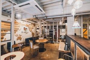 A modern cafe with exposed ductwork, wooden tables, and a mural on the wall. - Kotori Coworking & Hostel Takamatsu (Takamatsu)