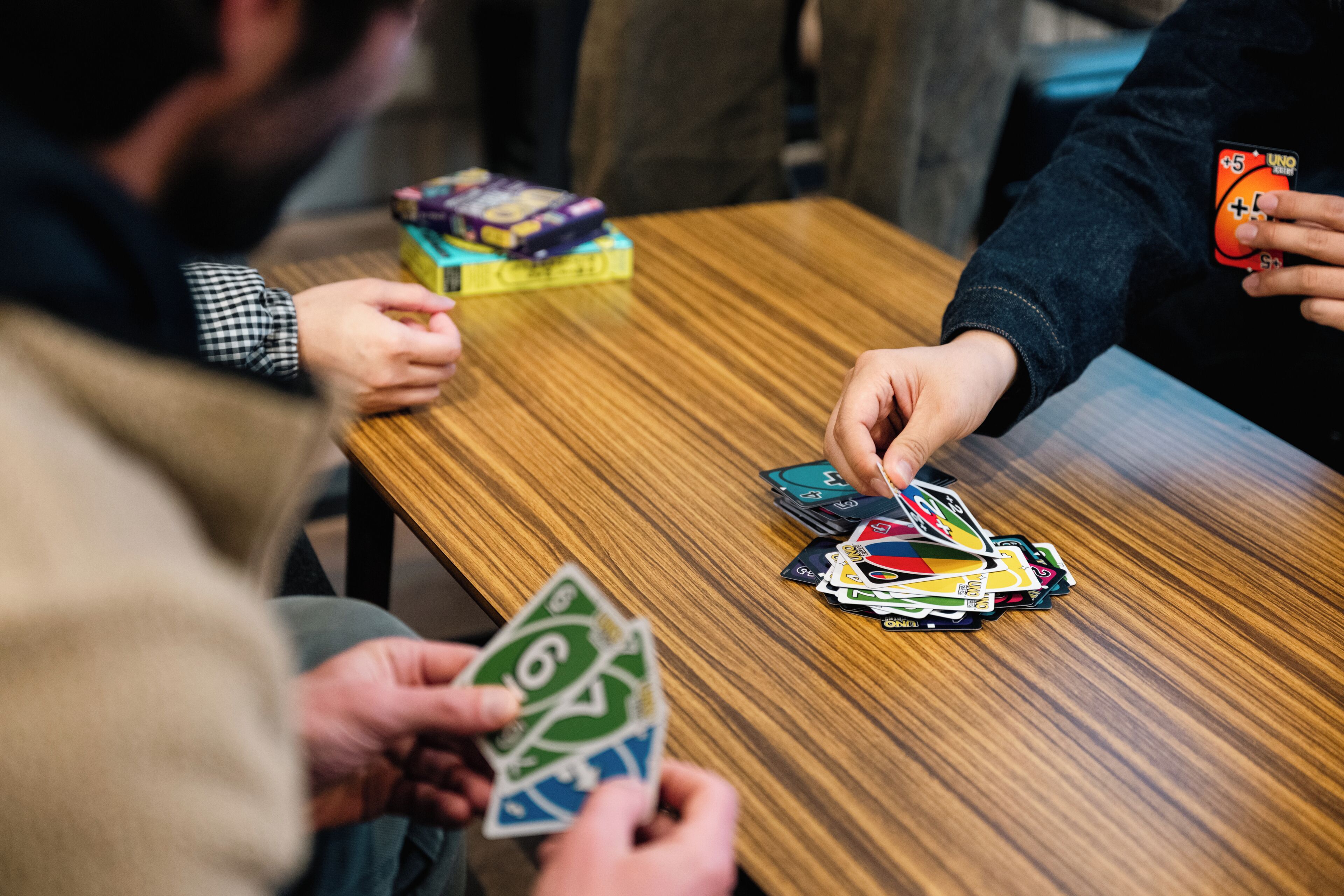 Una mesa de madera con un juego de cartas en curso, una caja de juegos y una persona sosteniendo una carta.
