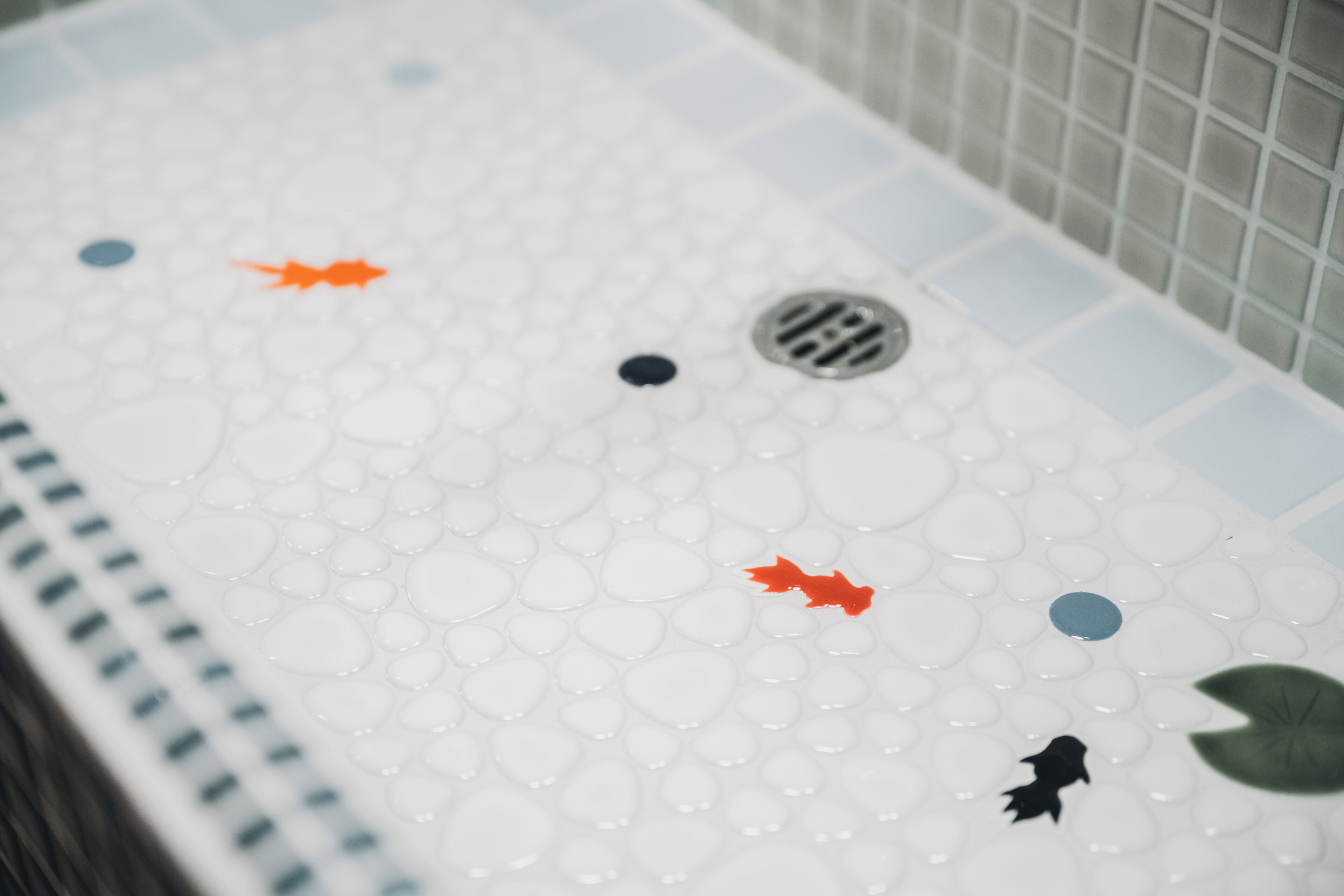 Una bañera con gotas de agua, desagüe y pared de azulejos.