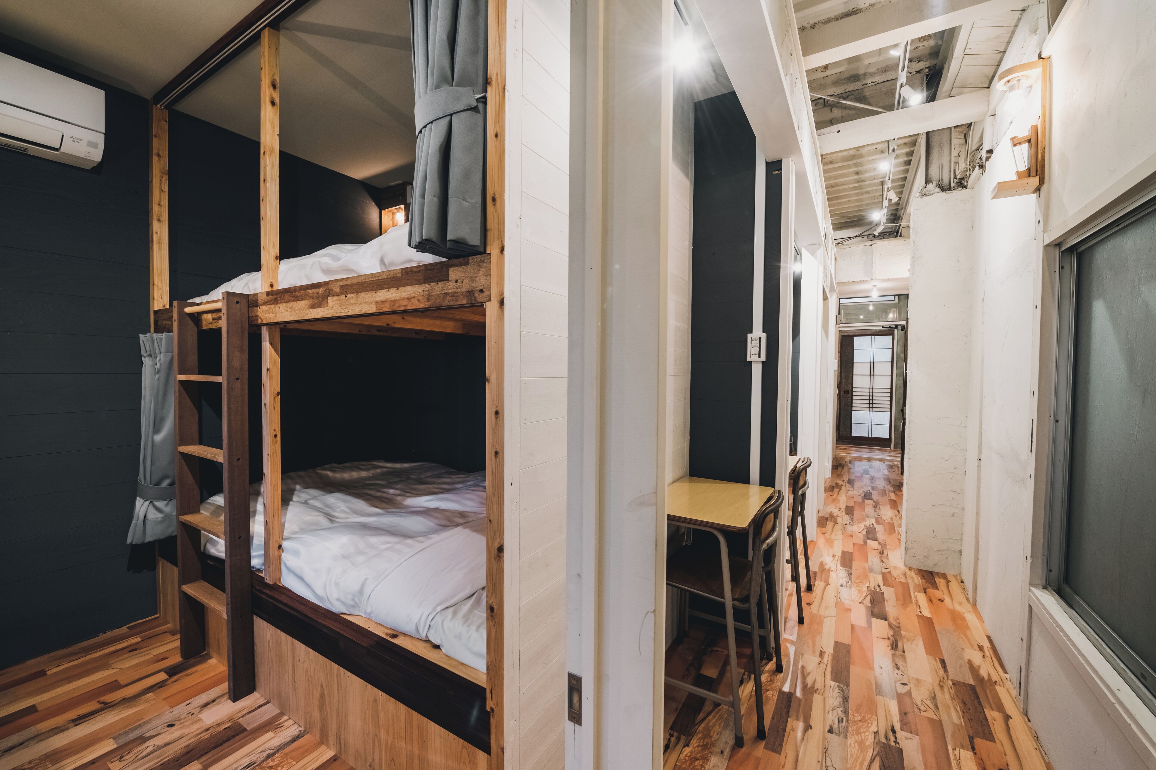 Habitación con literas, escritorio, silla, suelo de madera y ventana.