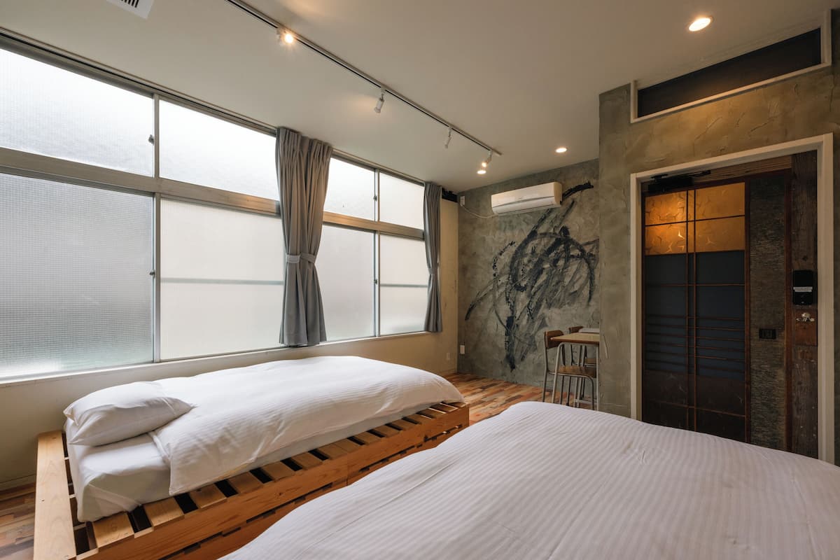 Habitación con dos camas, amplias ventanas con cortinas, pared de piedra con un diseño negro y un ascensor.