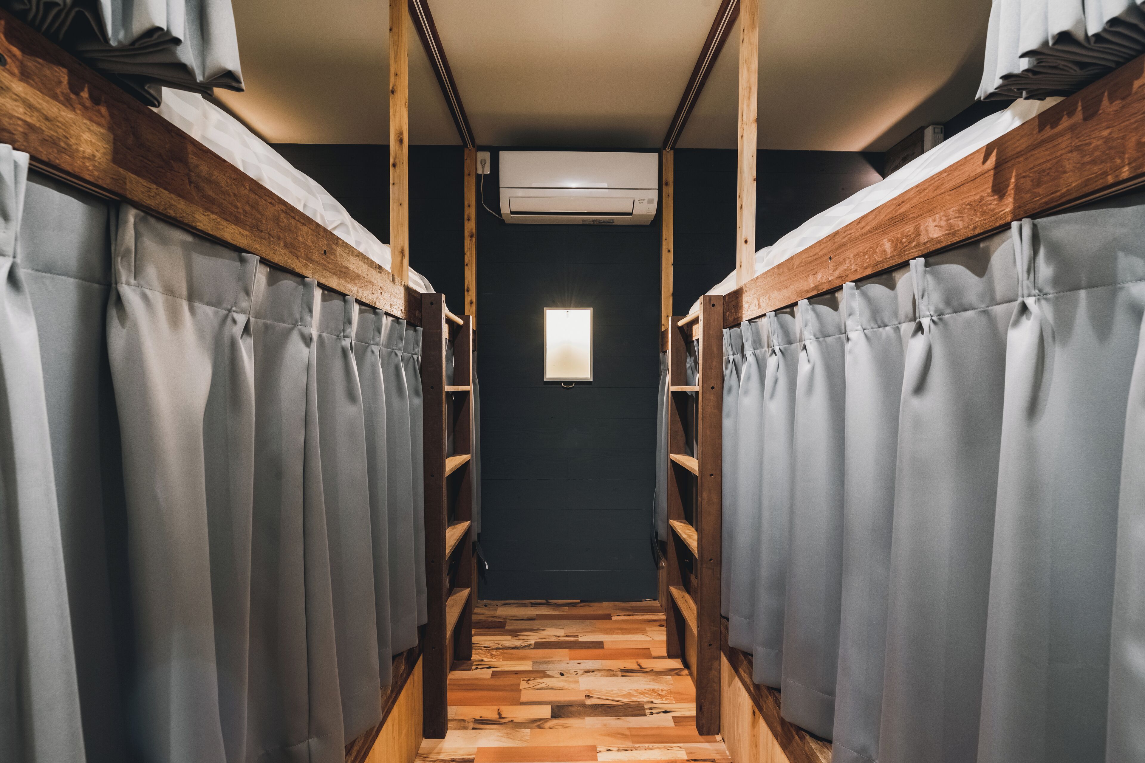 A narrow hallway with bunk beds on either side, wooden flooring, and a small window at the end.
