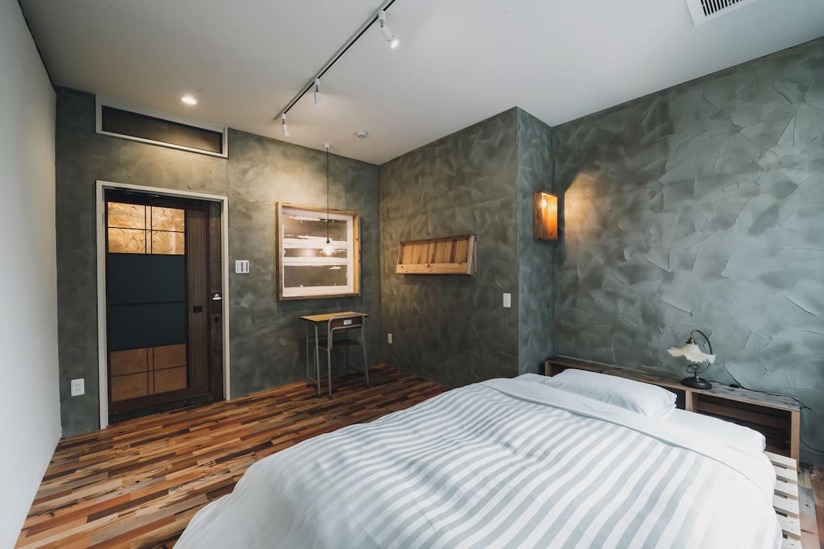 Un dormitorio con una cama grande, un escritorio de madera, una mesita pequeña y un estante en la pared.