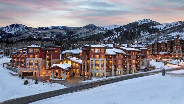 Un chalet à étages doté d’une façade en pierre, de nombreux balcons et, en arrière-plan, d’un paysage enneigé.