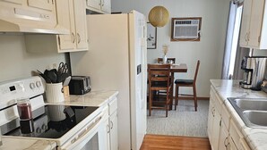 Una cocina con armarios blancos, estufa, refrigerador y un comedor con mesa y sillas.