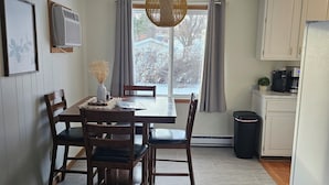 Un comedor con mesa y sillas de madera, una lámpara colgante, un cuadro en la pared y vistas al exterior a través de una ventana.