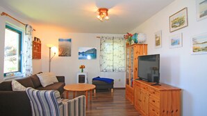 Un salon comprenant un canapé, un fauteuil, un téléviseur, un meuble en bois et des œuvres d’art accrochées aux murs.