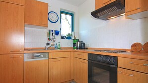 Une cuisine avec des meubles de rangement en bois, un lave-vaisselle, une cuisinière et une horloge au mur.