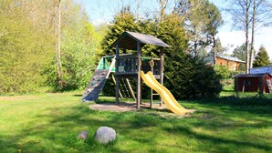 Une aire de jeux avec un toboggan et une structure d’escalade, entourée d’herbe et d’arbres.
