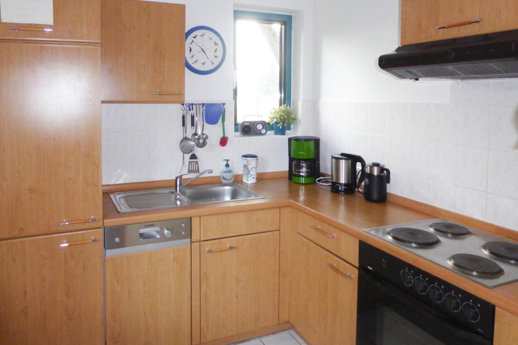 A kitchen with wooden cabinets, a sink, a stove, and a clock on the wall.