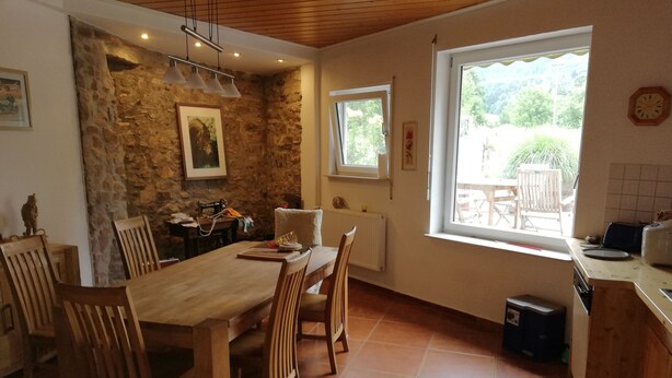 Una cocina amplia con una gran mesa de madera y sillas, una pared de piedra y una ventana con vistas a un jardín.