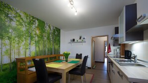 A dining area with a wooden table, chairs, and a bench. There is a wall mural of trees and a kitchen with a sink and cabinets. - Apartment 'Blomberg' with Shared Terrace and Wi-Fi (Meinerzhagen)