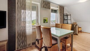 A dining area with a glass table and wicker chairs, a view through a patterned curtain, and a bookshelf against the wall.