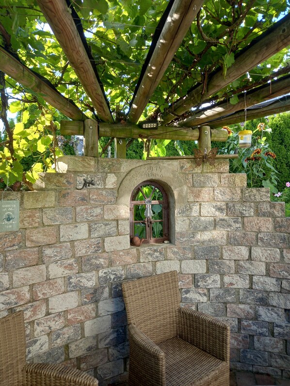 A stone wall with a wooden pergola, a rustic chair, and a small window.