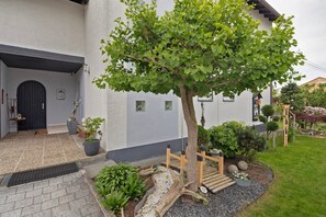 A house with a tiled entrance, a tree, a wooden fence, and a garden with various plants.