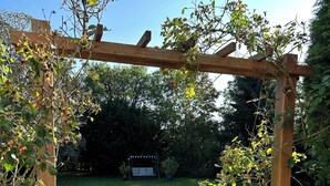 A wooden pergola with a stone lantern base, a grassy lawn, and a garden with potted plants.