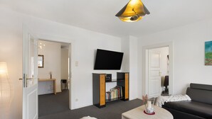 Un salon moderne comprenant un canapé, une table basse, un téléviseur à écran plat, une bibliothèque et une lampe.