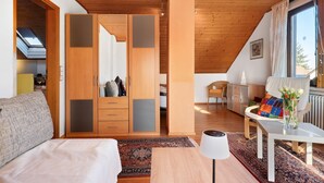 Ein Schlafzimmer mit Holzbalkendecke, einem Kleiderschrank, einem Bett, einem Tisch mit Lampe und Blick ins Freie.