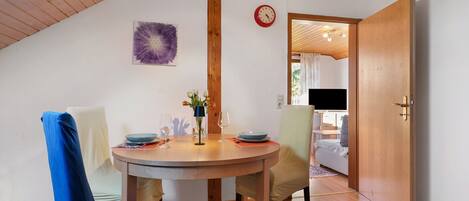 A dining area with a round table, chairs, a clock, and a door leading to another room.