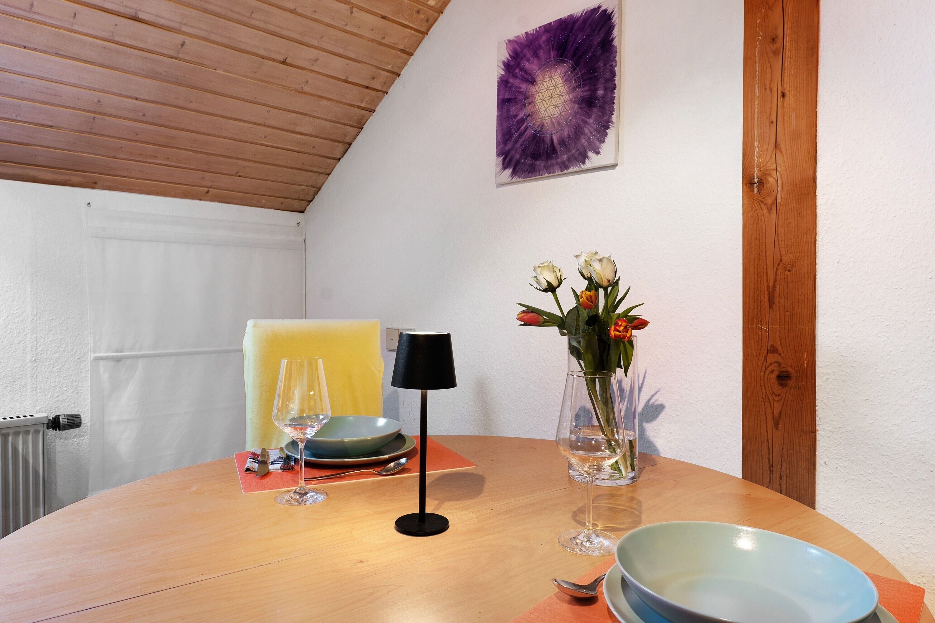 A round dining table with a vase of flowers, wine glasses, plates, and a black lamp.