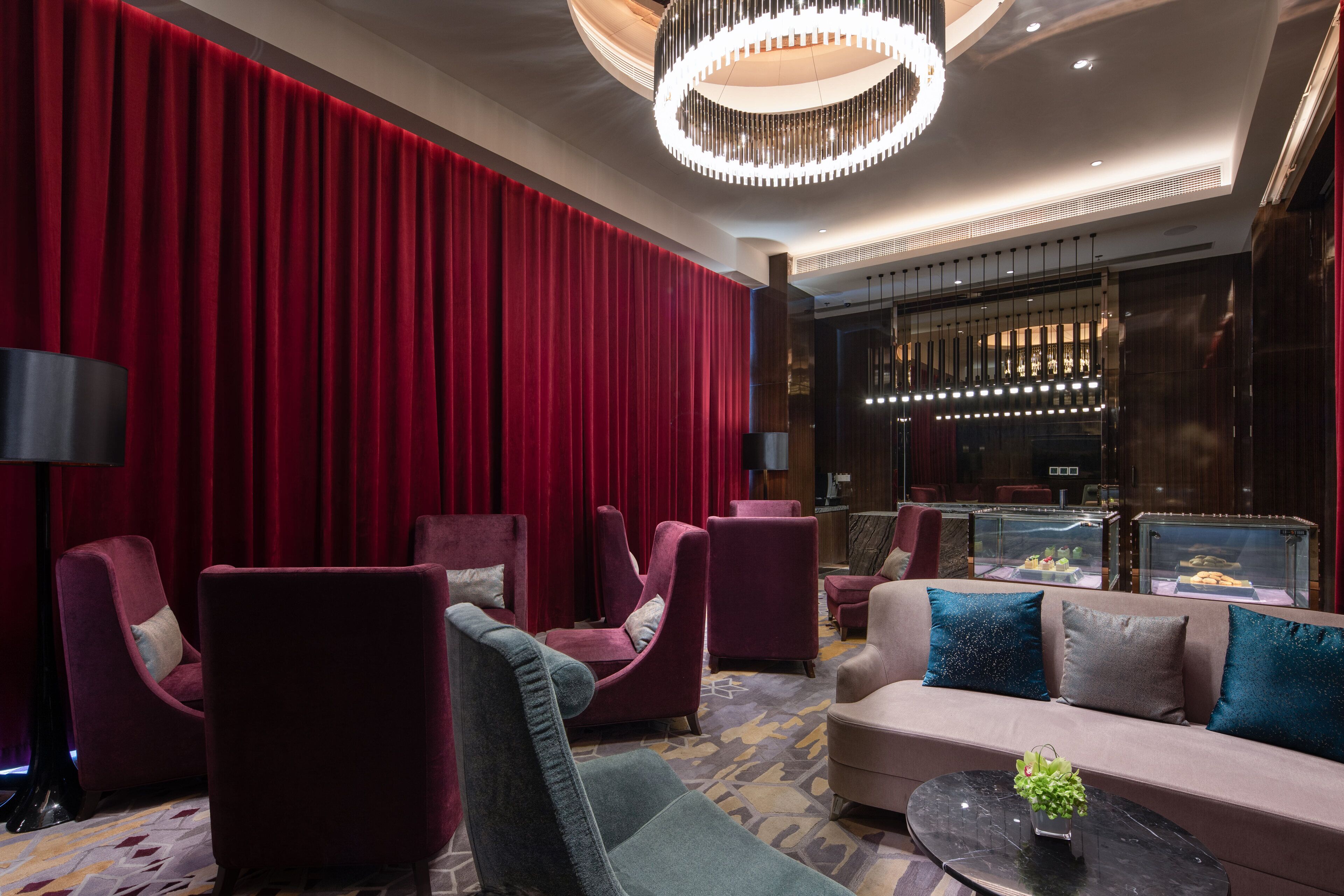 A modern lobby with red curtains, plush seating, a chandelier, and a glass display case.