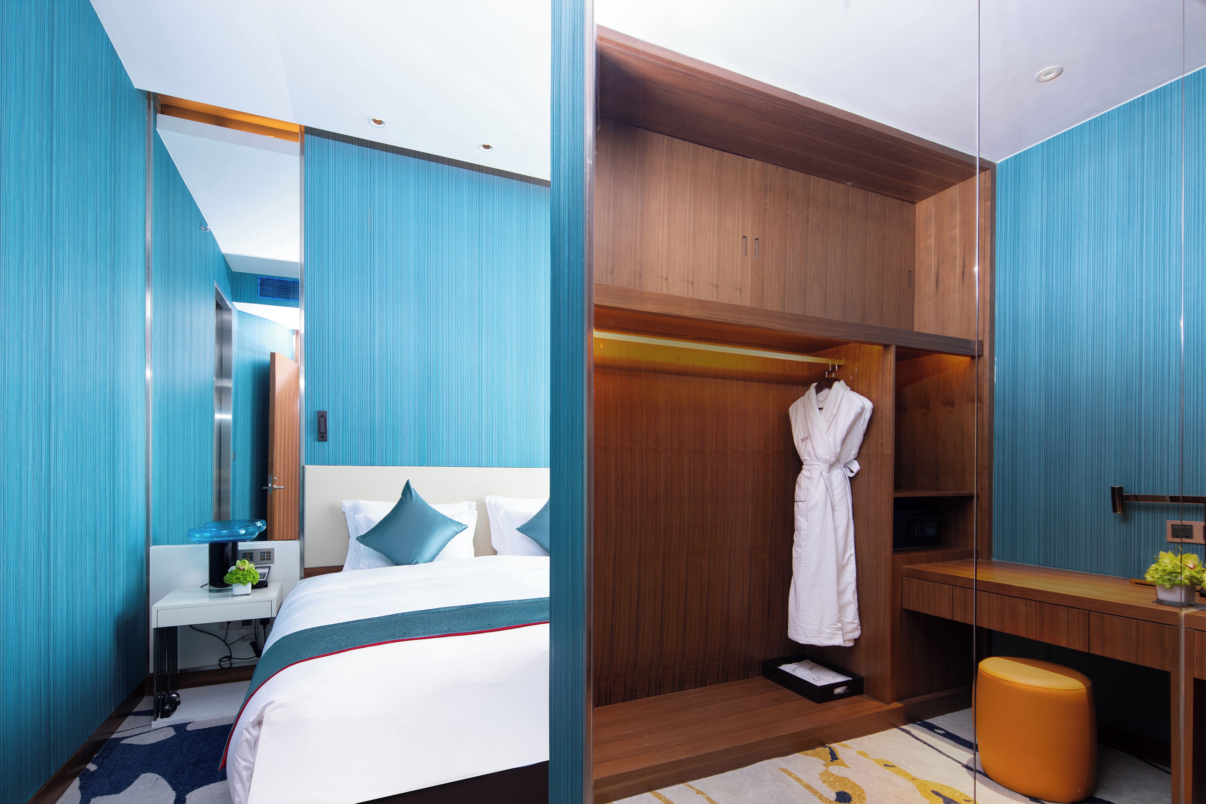 A modern hotel room with a large bed, a wooden wardrobe, a desk, and a bathroom area.