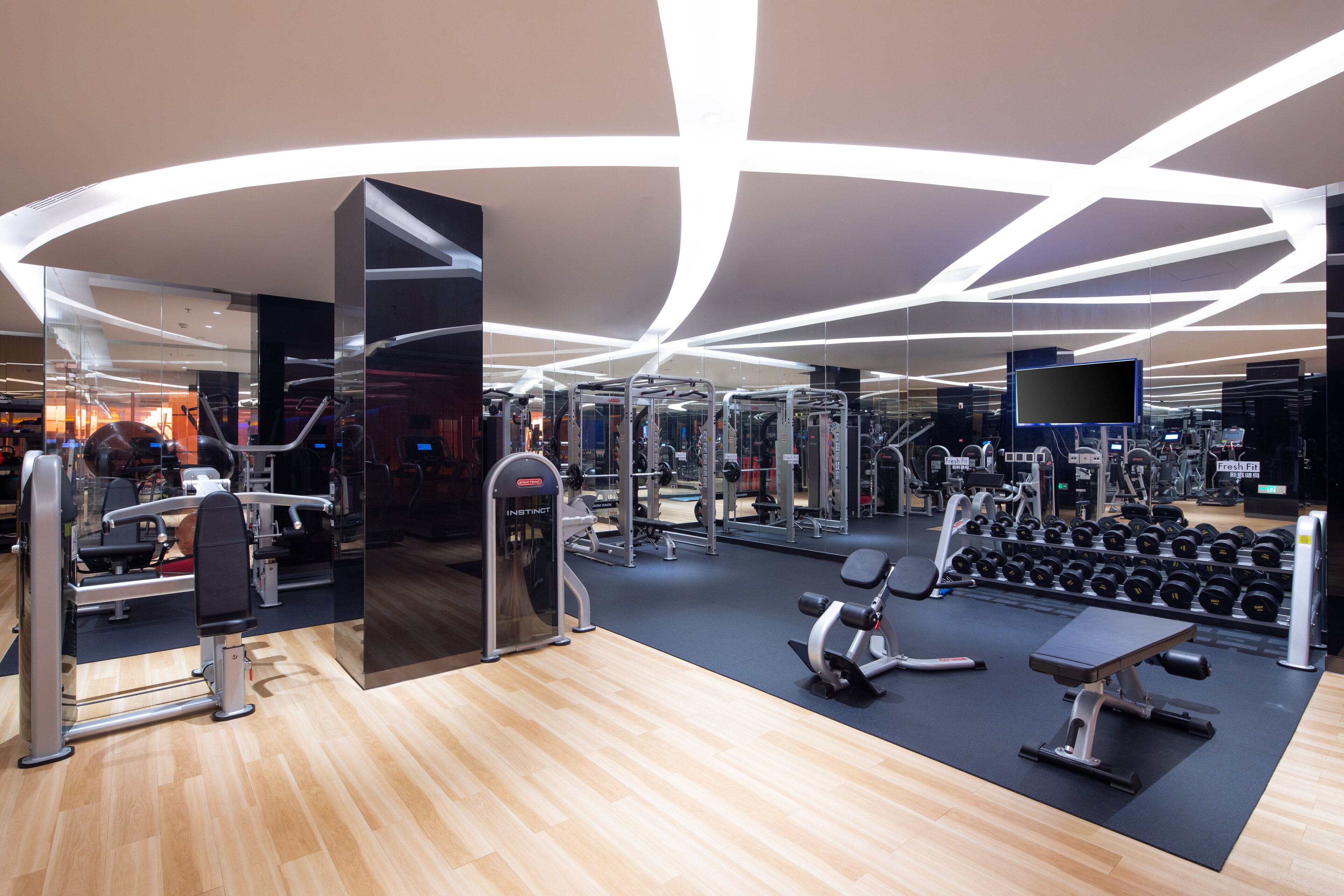 Une salle de sport moderne équipée de divers appareils d’exercice, dotée d’un mur miroir et d’un plancher en bois.