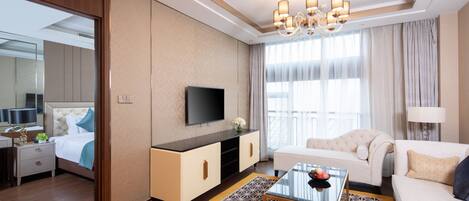 A modern hotel room with a large bed, a TV, a sofa, a coffee table, and a chandelier.