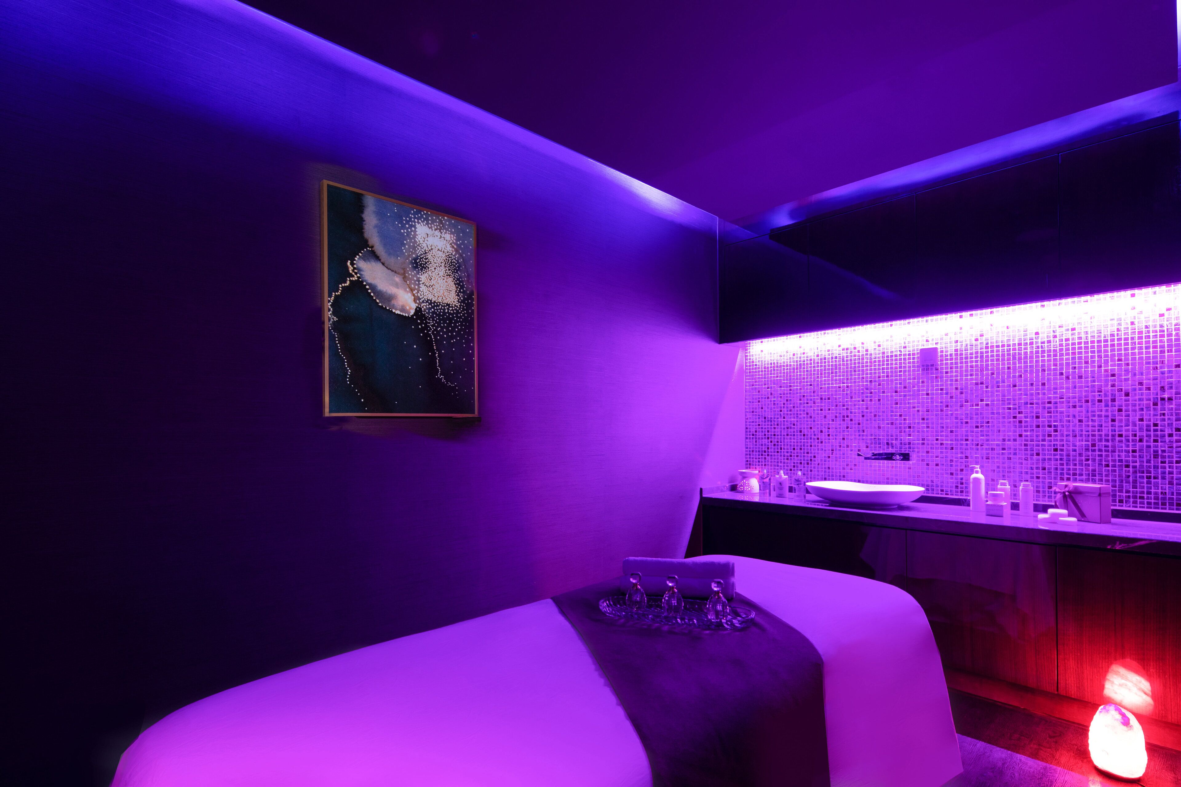 Une salle de bain moderne avec un mur éclairé en violet, un grand miroir et un espace lavabo.